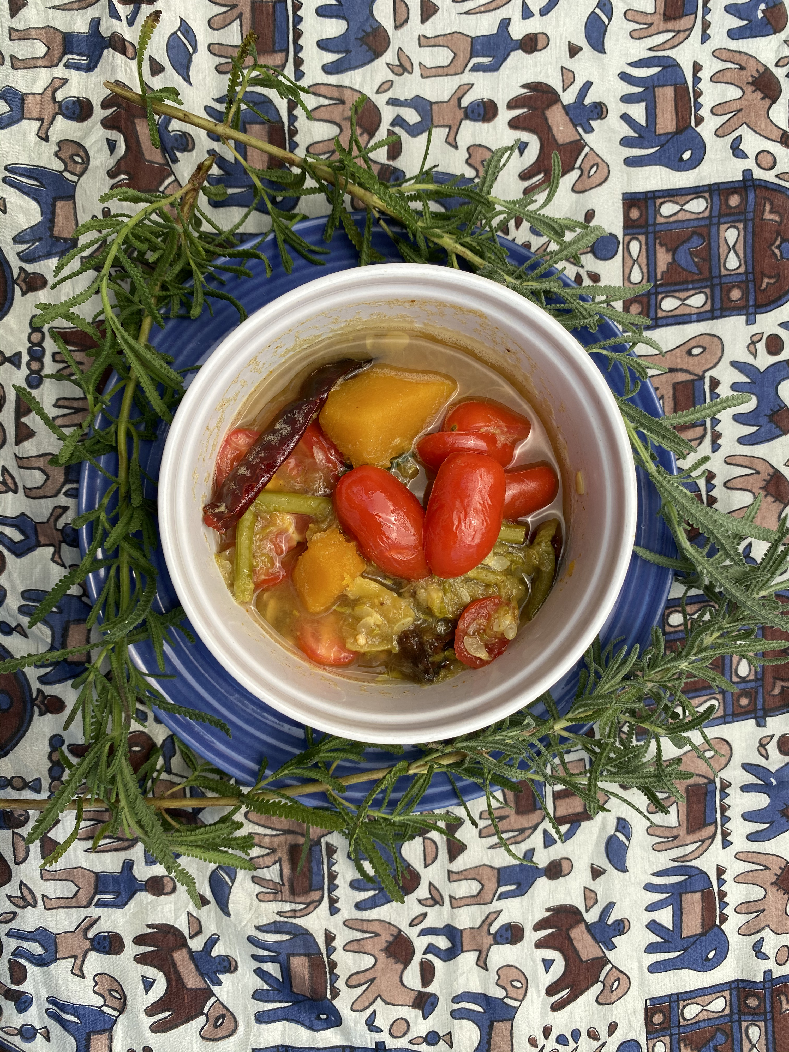 Sambar served in a white bowl. Leaves as a decorative element, against multi-colored tablecloth.