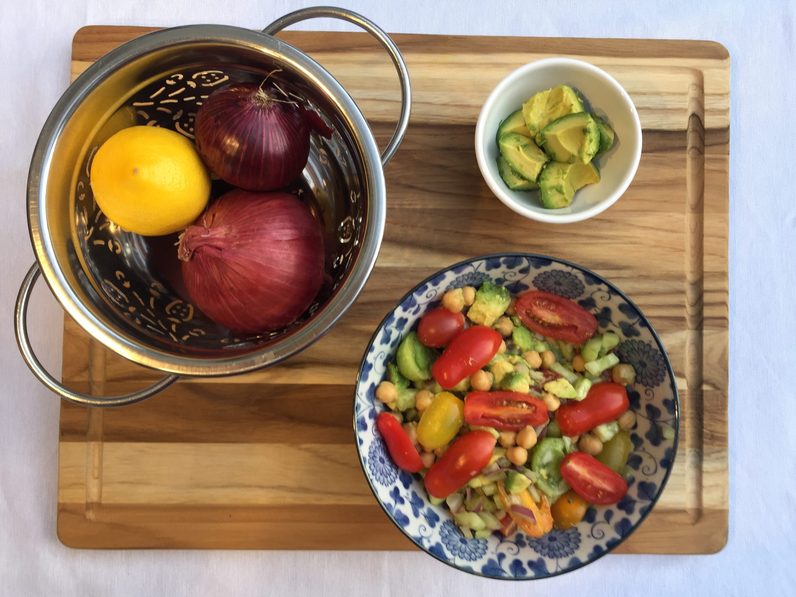 Yami’s Chickpea Salad in a blue-and-white bowl. Silver bowl containing two red onions and a lemon. Small white bowl containing pieces of avocado.