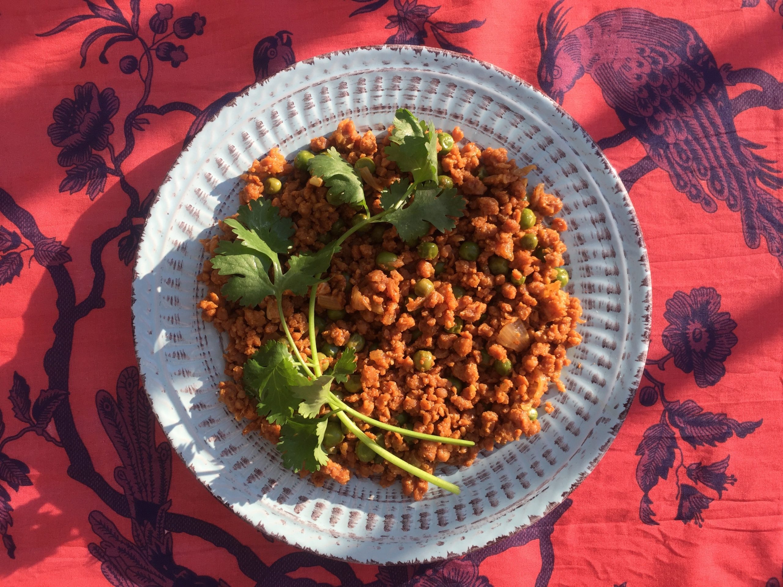 Vegan Keema Matar served on a blue plate against a red-and-purple printed tablecloth.