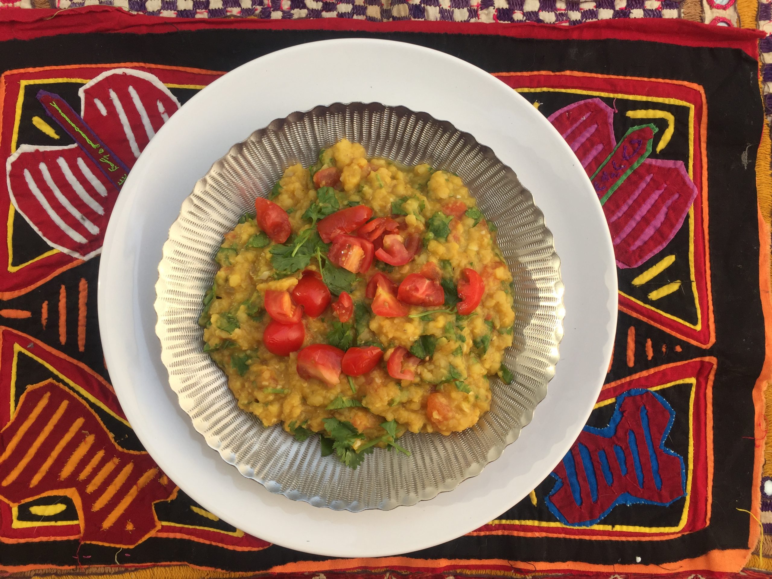 A bowl of lentils with tomatoes and chopped greens on top, sitting on a colorful butterfly placemat.